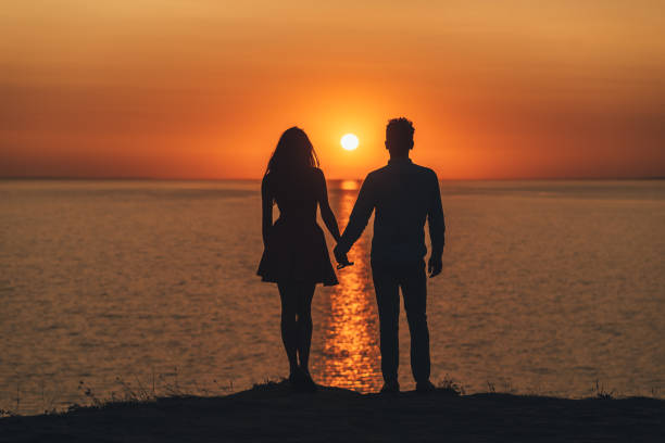 The romantic couple standing on the sea shore on the beautiful sunset background